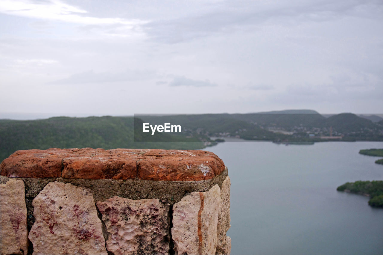 Retaining wall by river and mountains against sky