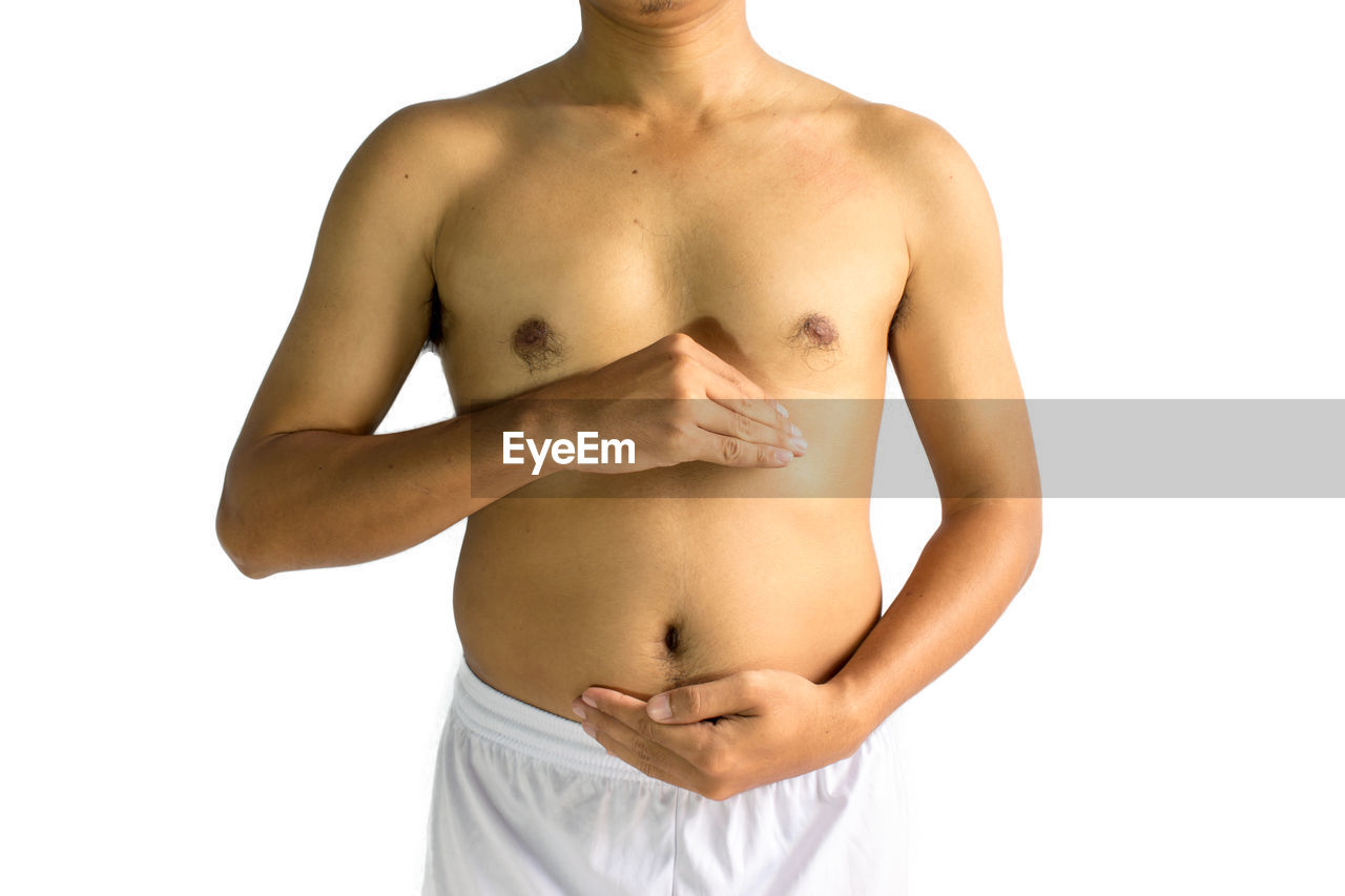 Midsection of shirtless young man touching belly while standing against white background
