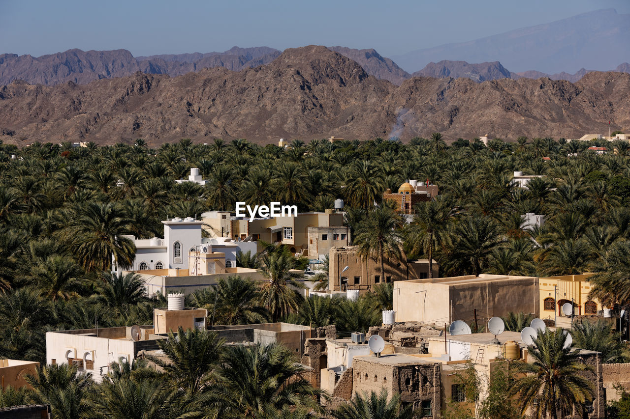 High angle view of buildings and palm trees with mountains against sky