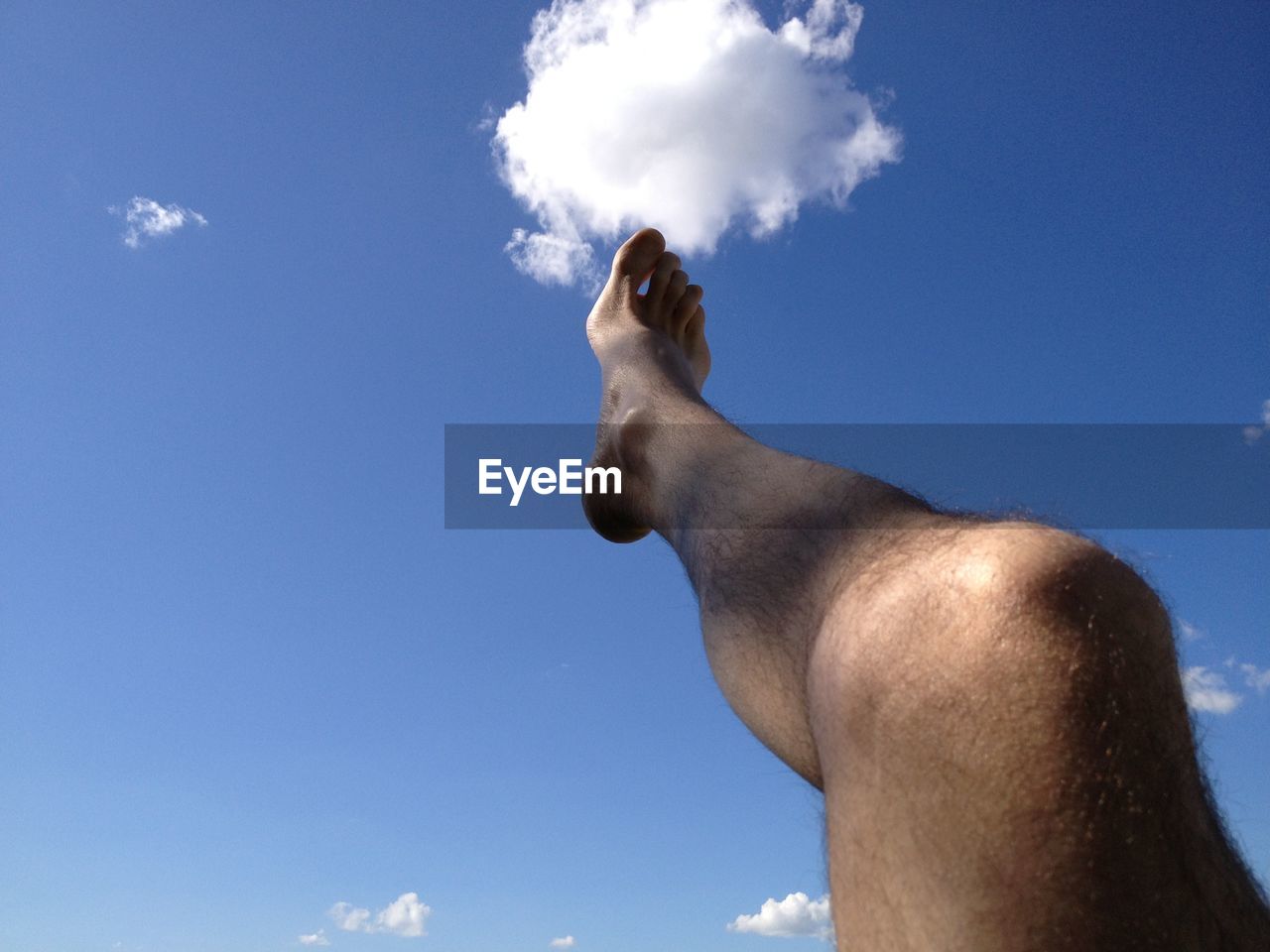 Low section of man leg up in air against blue sky