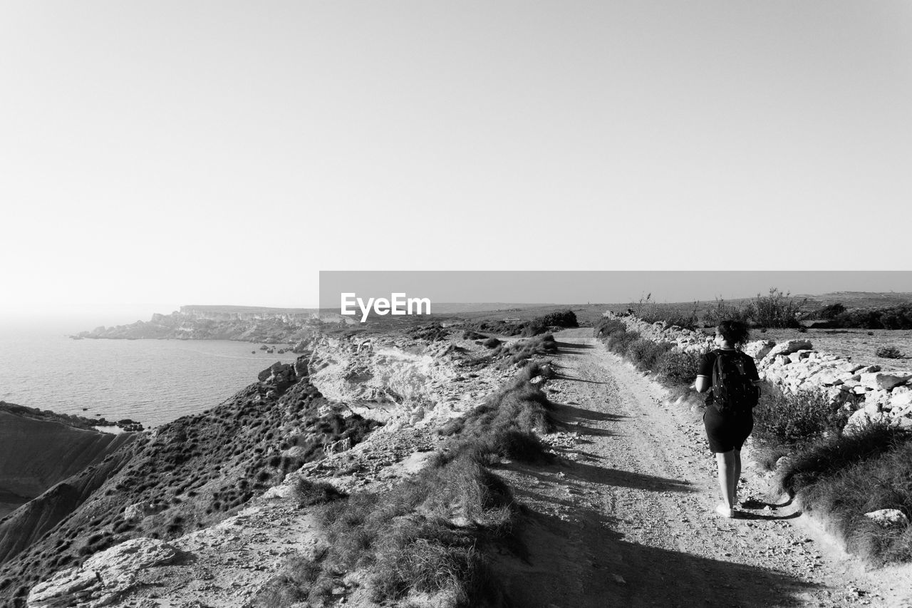 Rear view of woman hiking on mountain by sea against clear sky