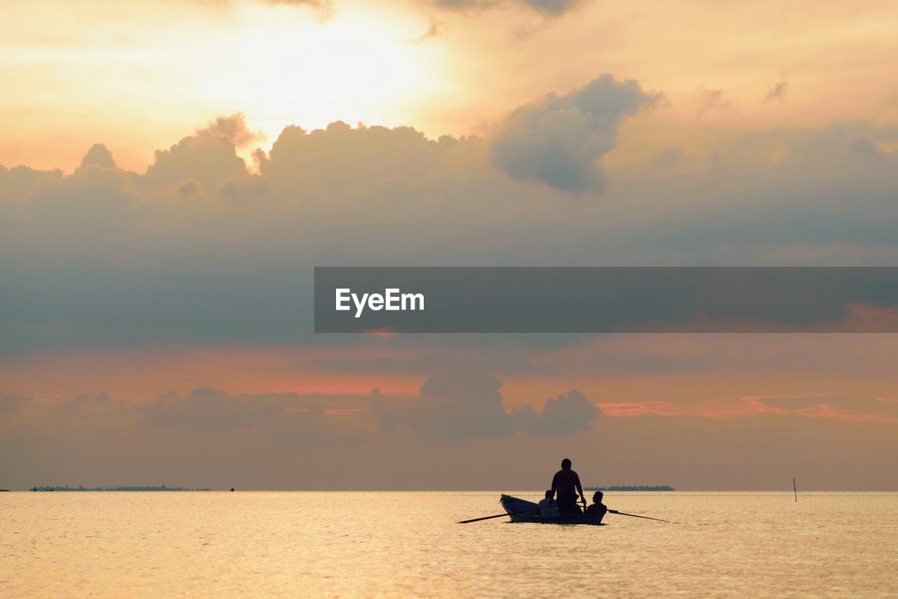 Silhouette men on boat sailing in sea against sky during sunset