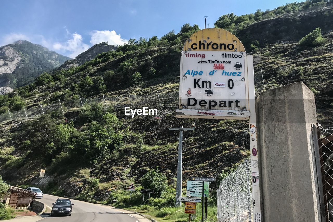 INFORMATION SIGN BY ROAD AGAINST MOUNTAINS