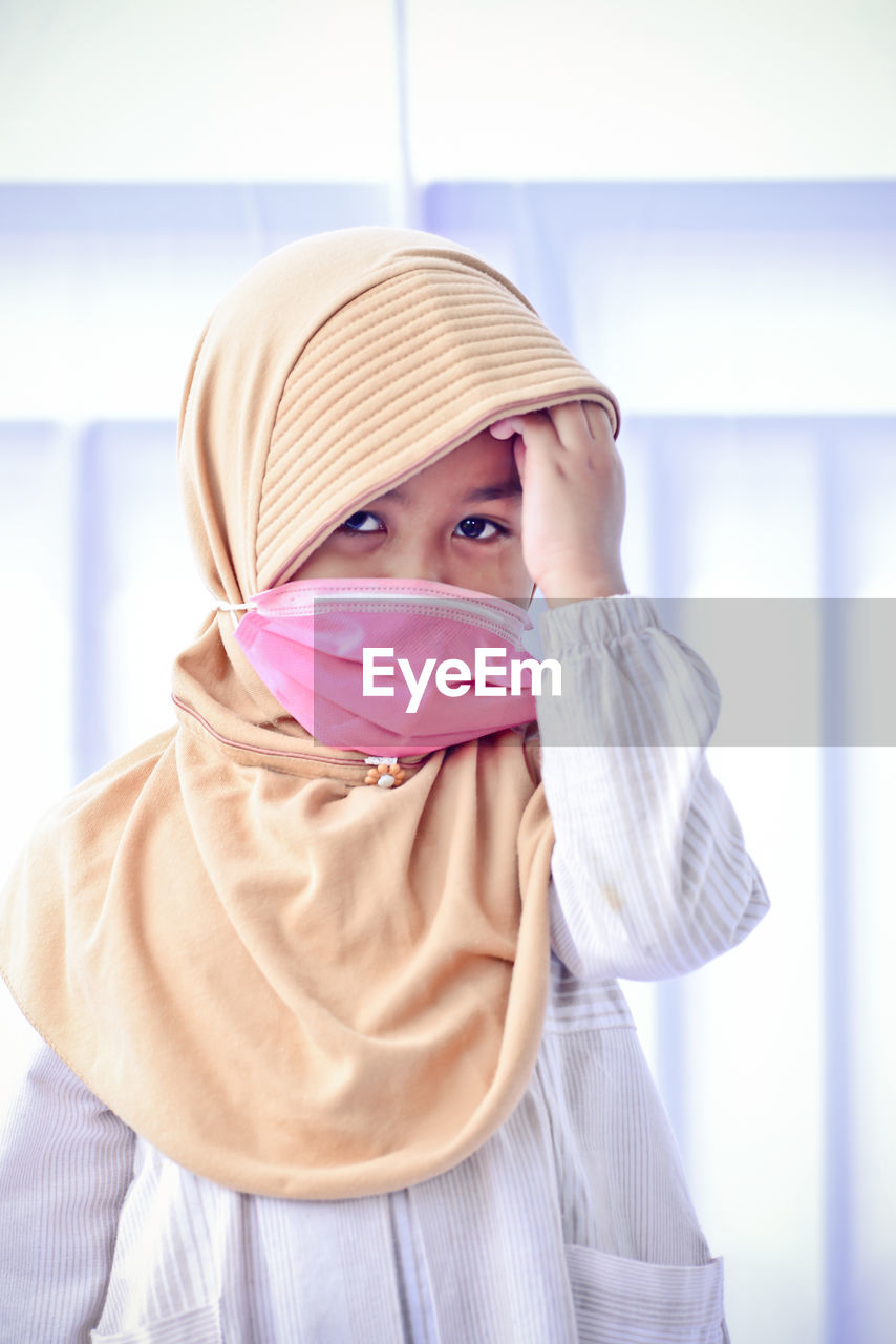 Portrait of cute girl wearing mask standing at home