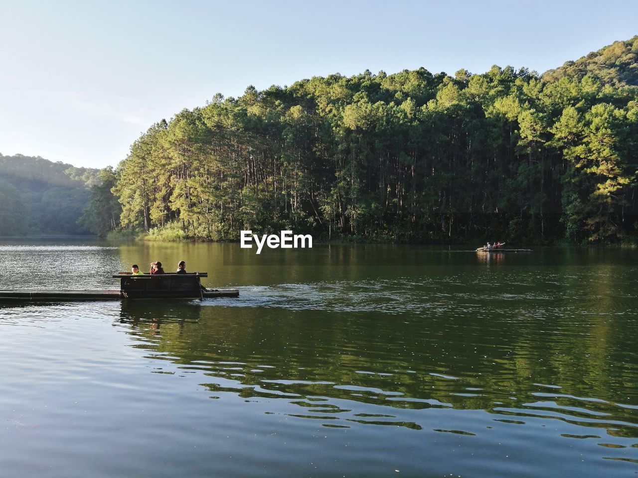 People on wooden raft in lake against trees