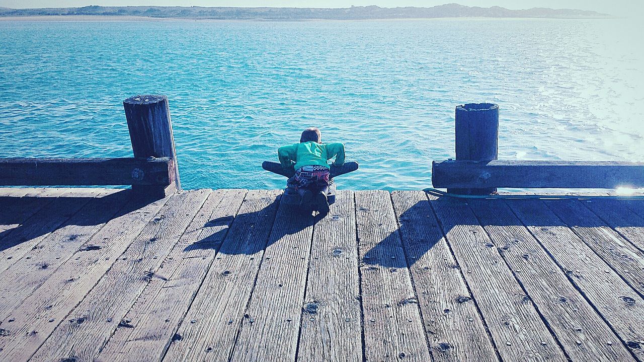 Rear view of boy leaning on bollard at pier in sea