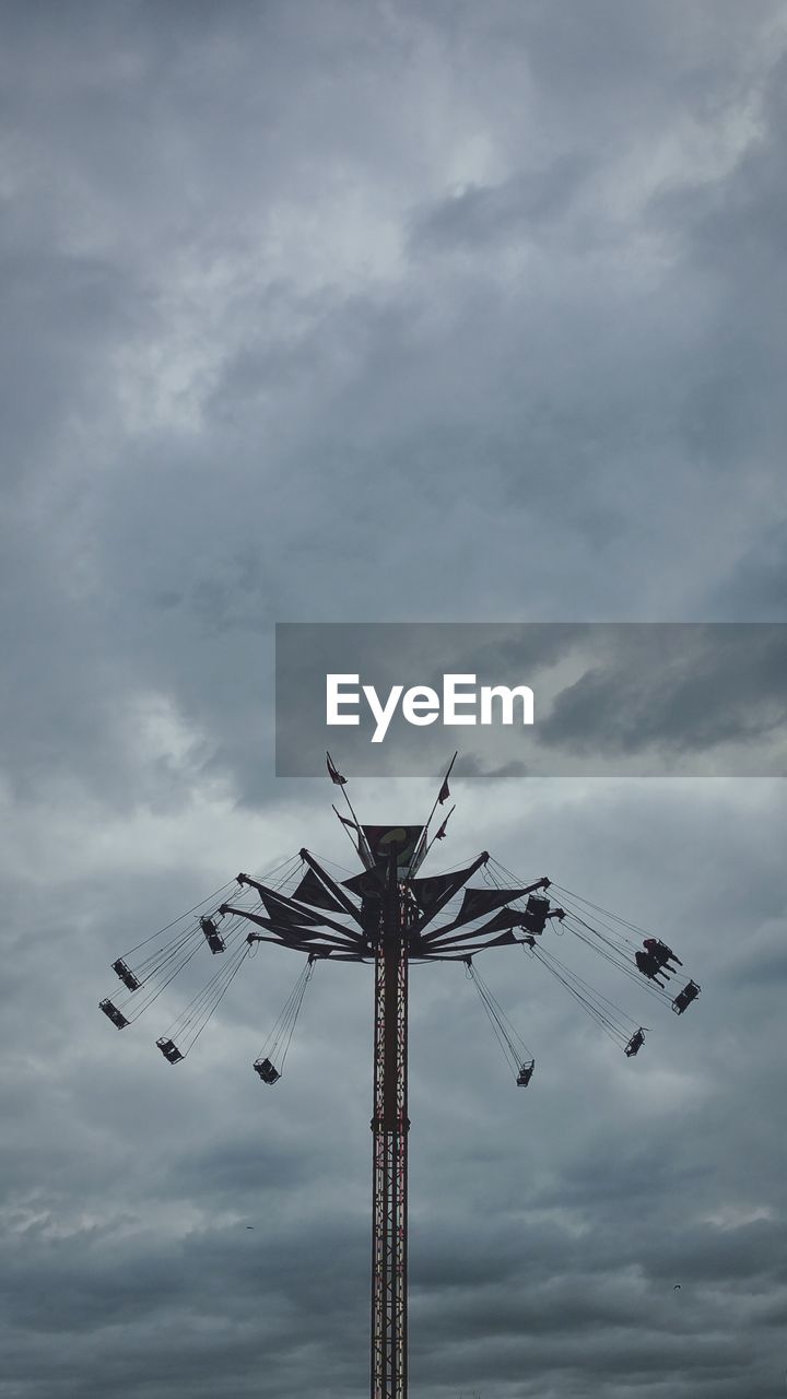 Low angle view of amusement ride spinning against cumulus cloud
