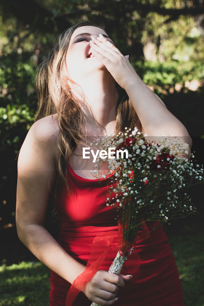 female, women, one person, red, adult, dress, nature, plant, long hair, young adult, hairstyle, flower, person, clothing, photo shoot, portrait photography, emotion, waist up, portrait, outdoors, standing, lifestyles, holding, fashion, sunlight, flowering plant, day, summer, blond hair, tree, brown hair, eyes closed, leisure activity, beauty in nature, three quarter length
