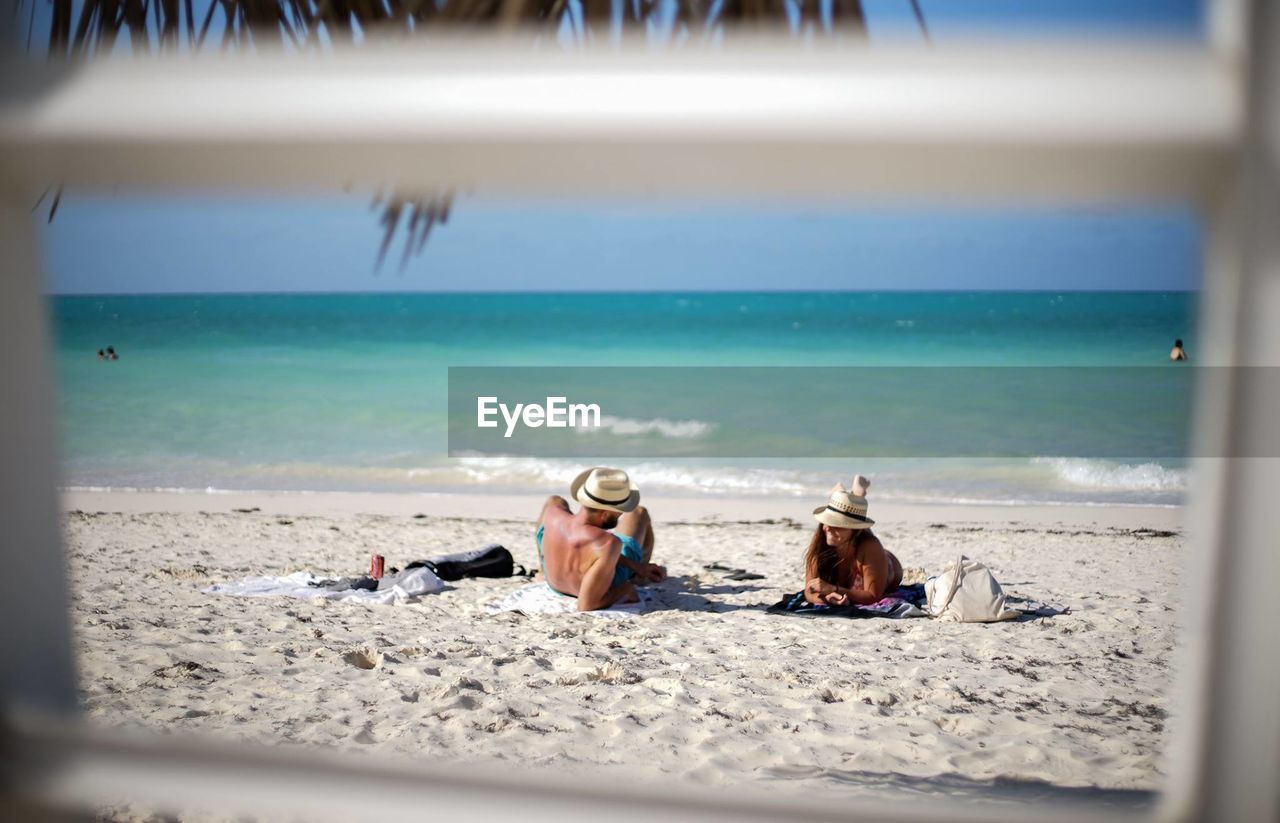 Man and woman relaxing at beach seen through railing