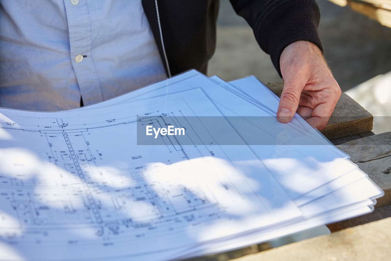 Midsection of architect with blueprints at table on sunny day