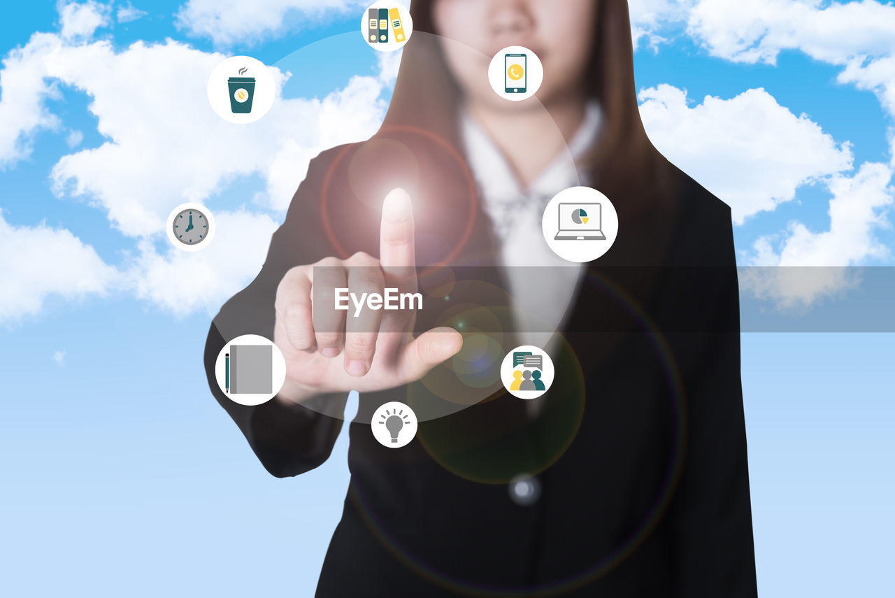 Midsection of businesswoman touching icons on digital display against blue sky