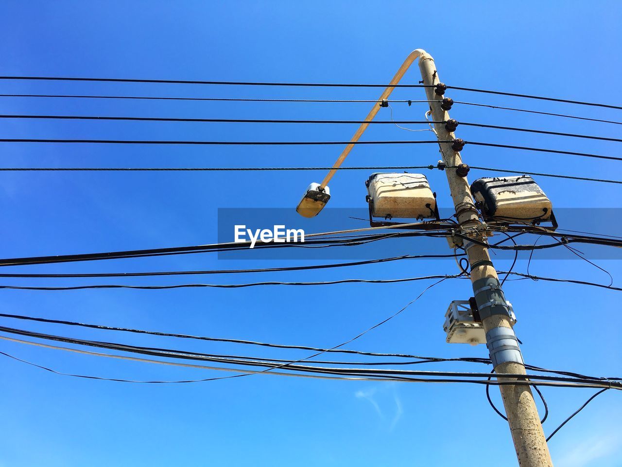 Low angle view of street light with electricity cables against blue sky