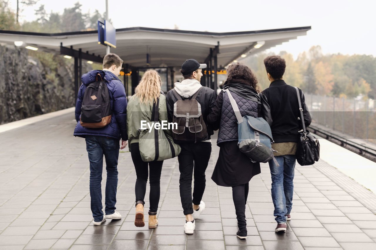 Full length rear view of university students walking together on subway platform