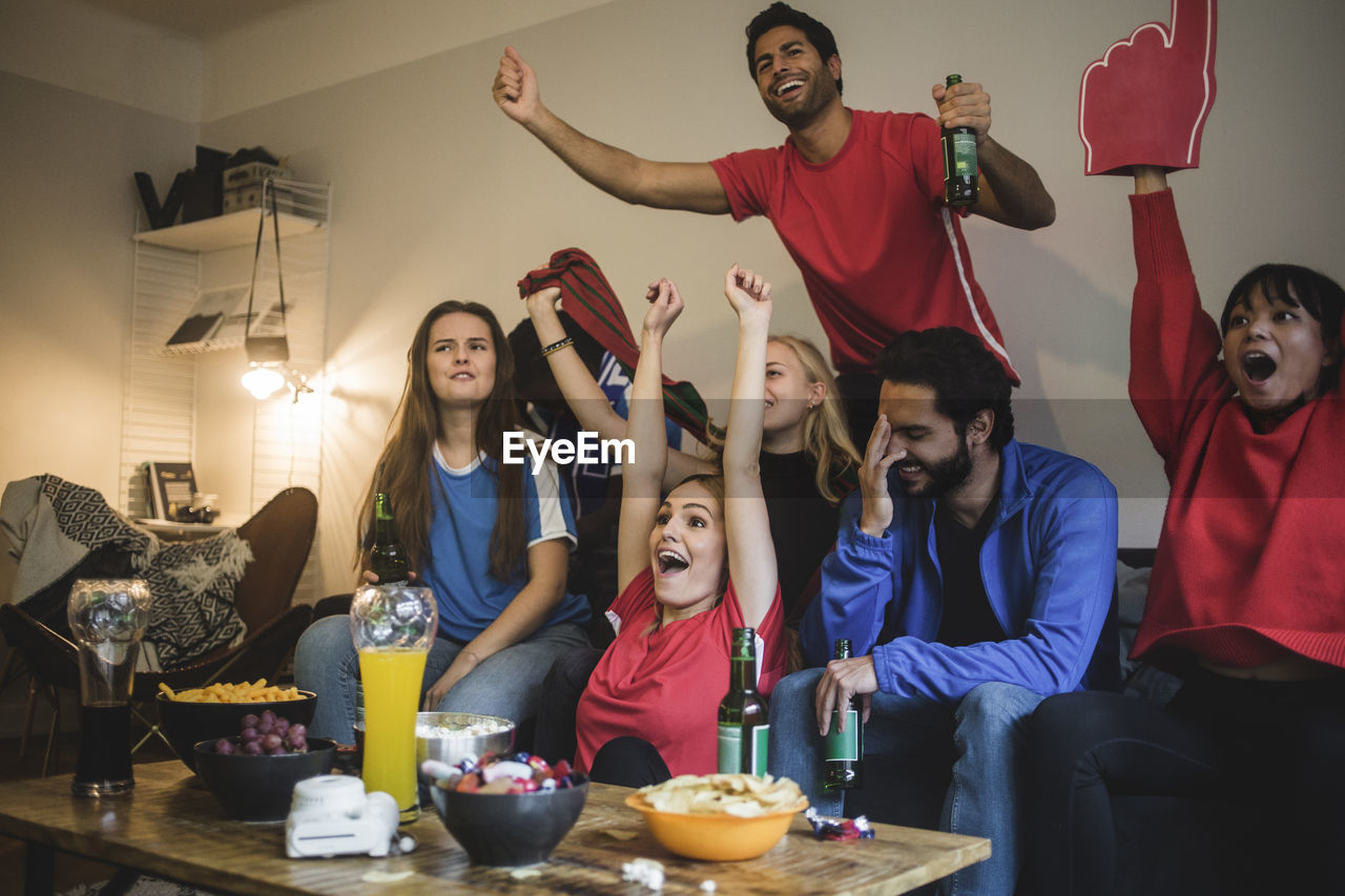 Multi-ethnic friends watching sport while sitting on sofa at home