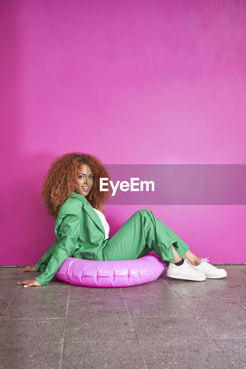 Happy businesswoman sitting on inflatable ring in front of pink wall