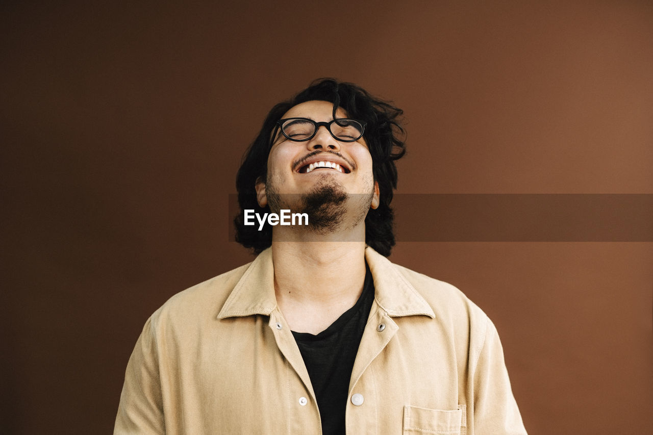 Cheerful man with eyes closed against brown background