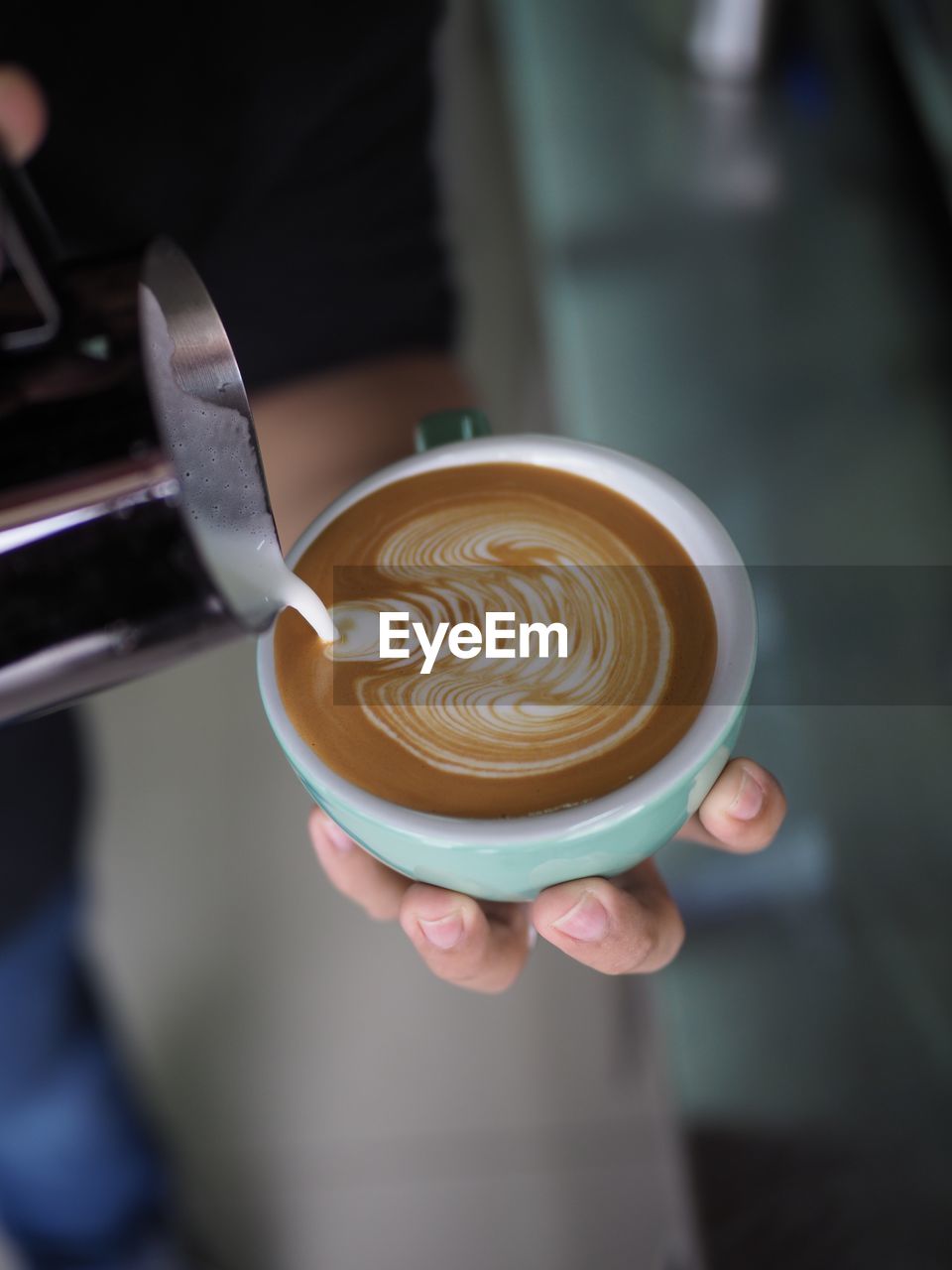 Cropped hand of person pouring milk in cappuccino