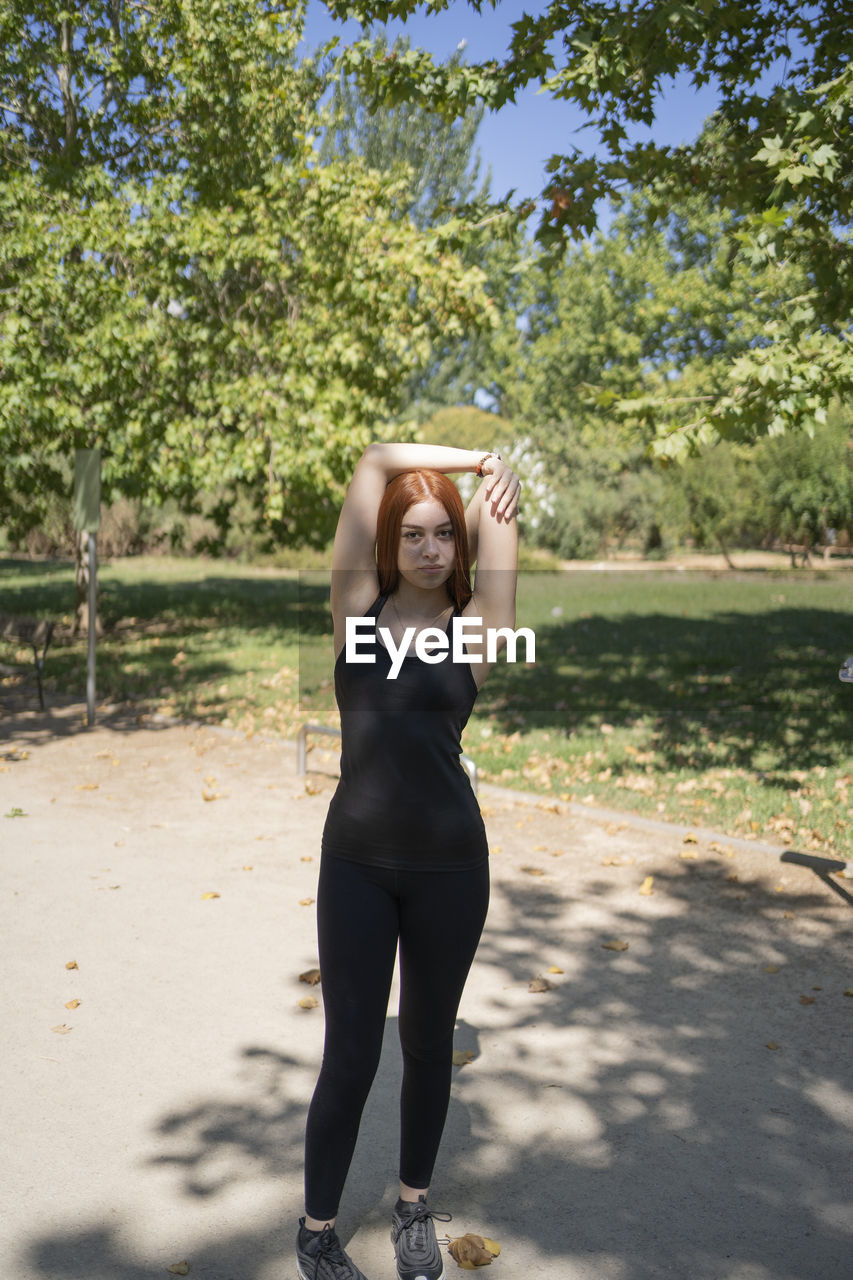Young redhead athlete stretching in a park before running outdoors in summer. person