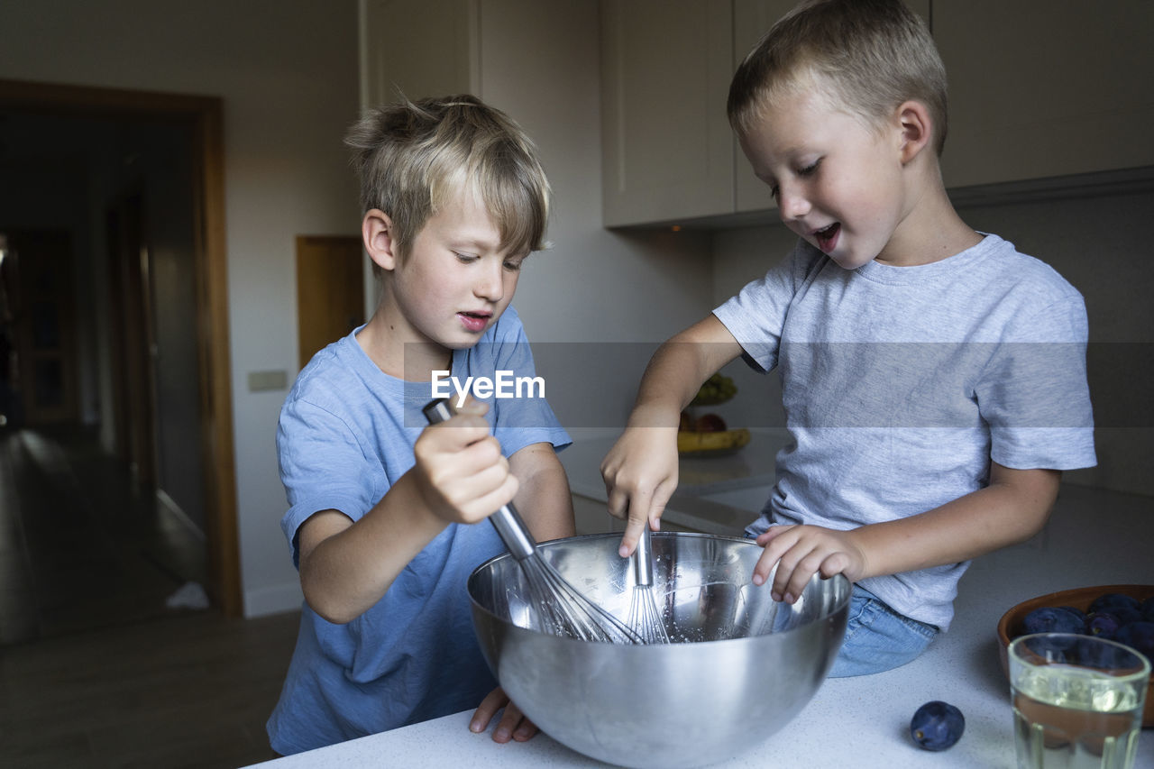 Brothers mixing cake batter in kitchen at home