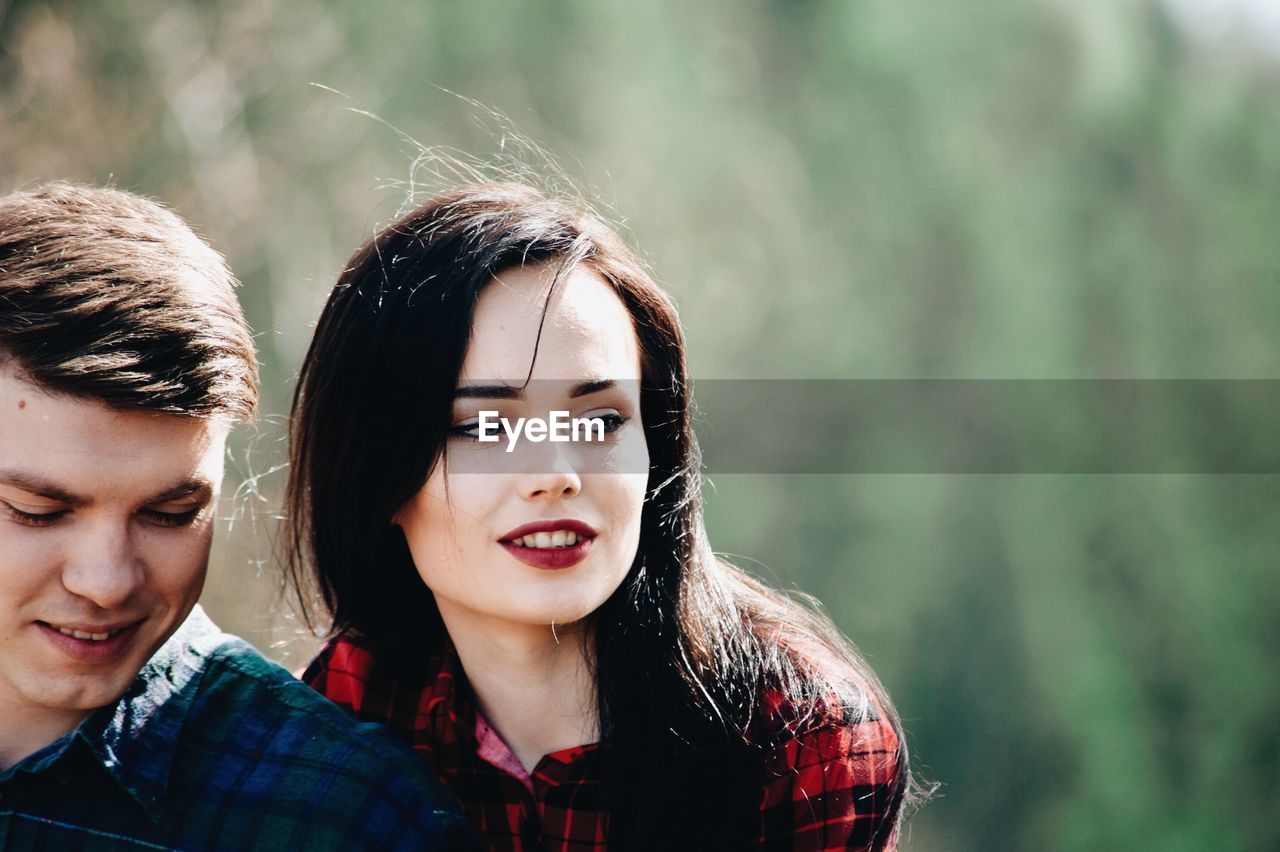 Young couple looking away in forest during sunny day