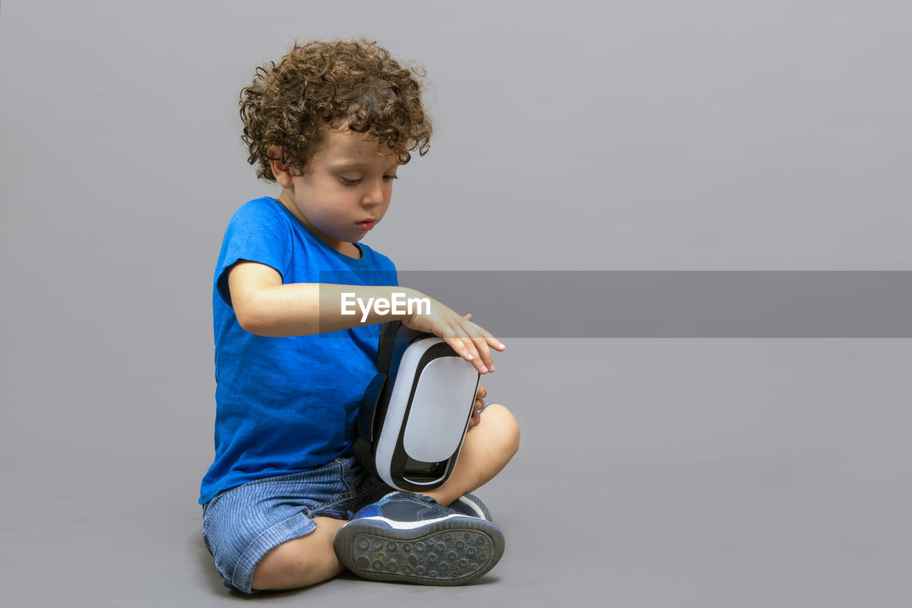 Little boy with virtual reality goggles in his hands looking curiously at how they work