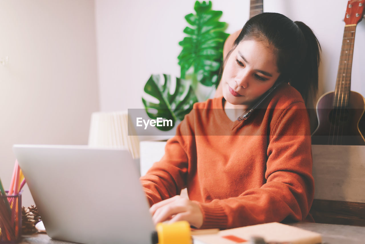 Woman talking over mobile phone while using laptop at home