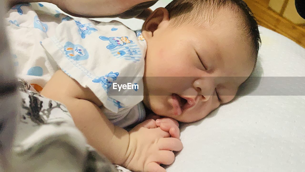 HIGH ANGLE VIEW OF CUTE BABY SLEEPING ON BED