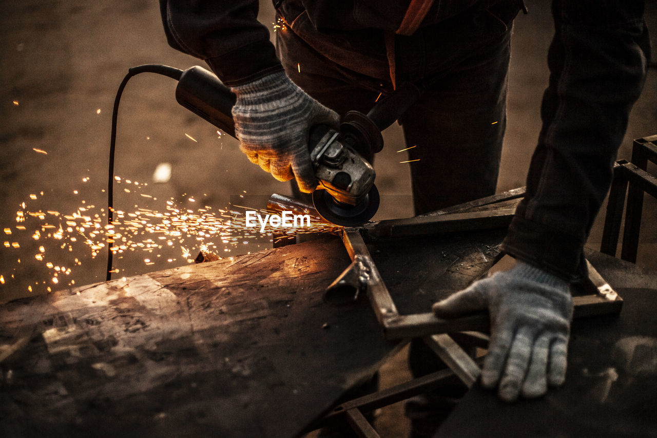 Midsection of worker grinding metal in factory