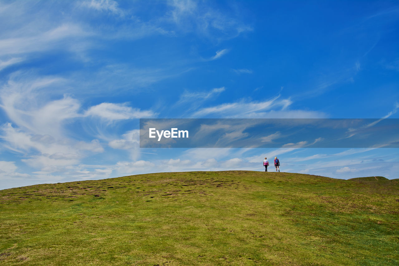 Two distant tourists walking on green hill