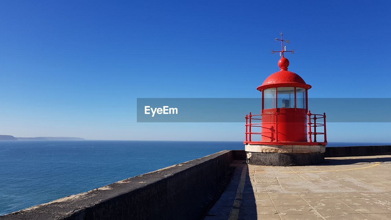 Lighthouse by sea against clear blue sky