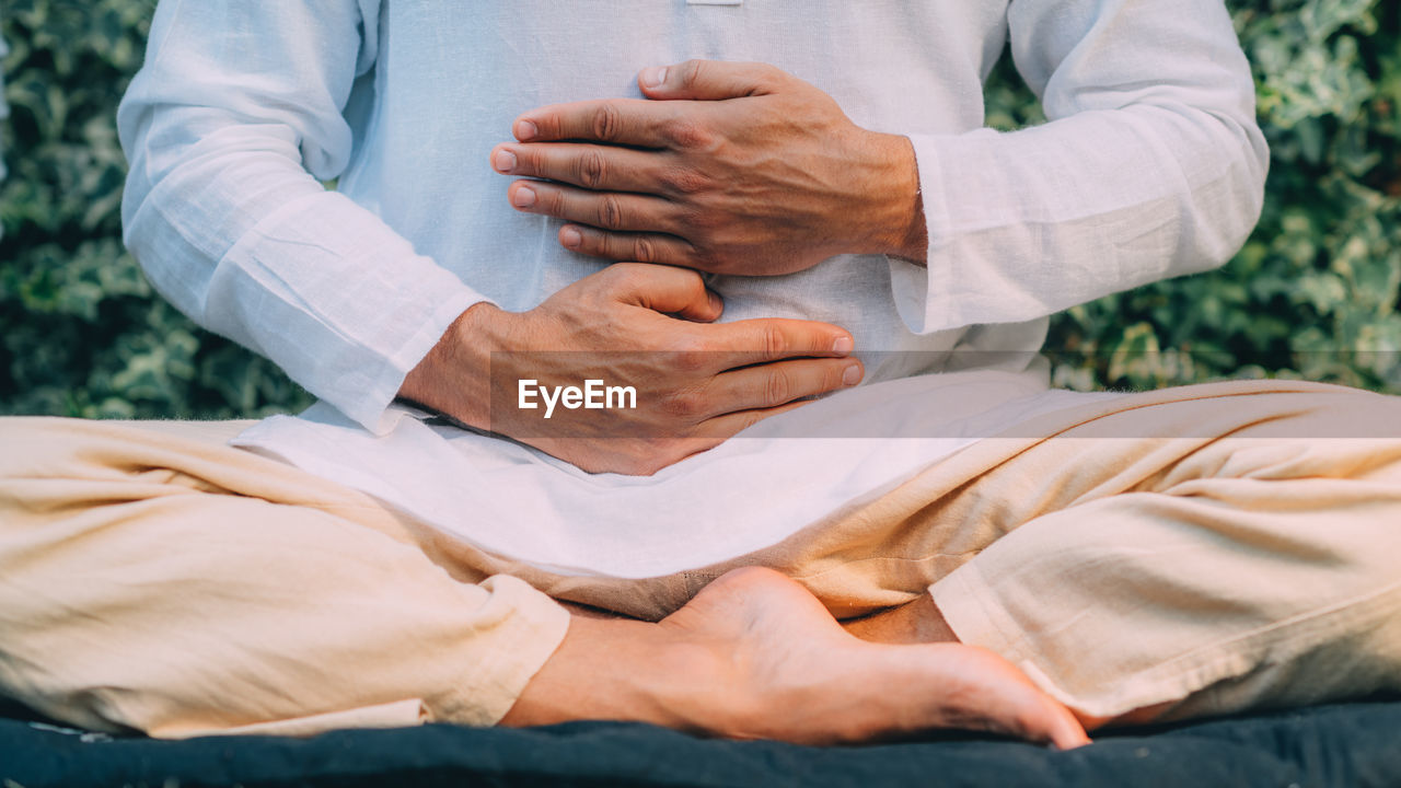Male therapist performing reiki therapy self treatment holding hands over his stomach. 