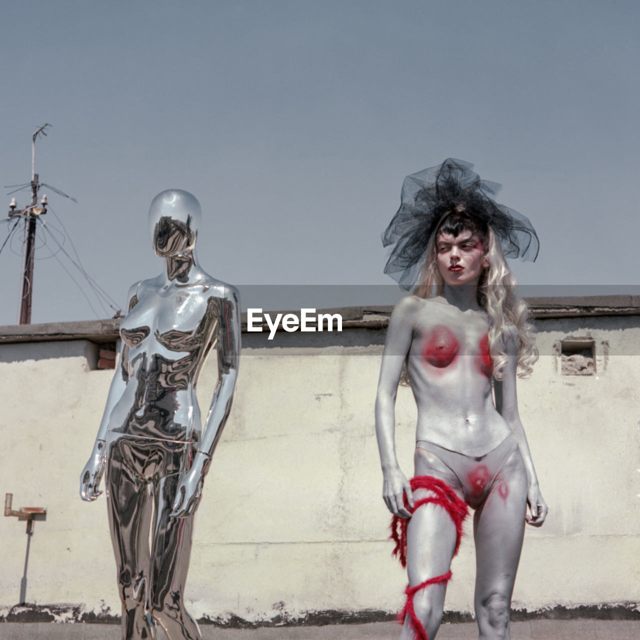 Naked woman with body paint standing against mannequin against sky