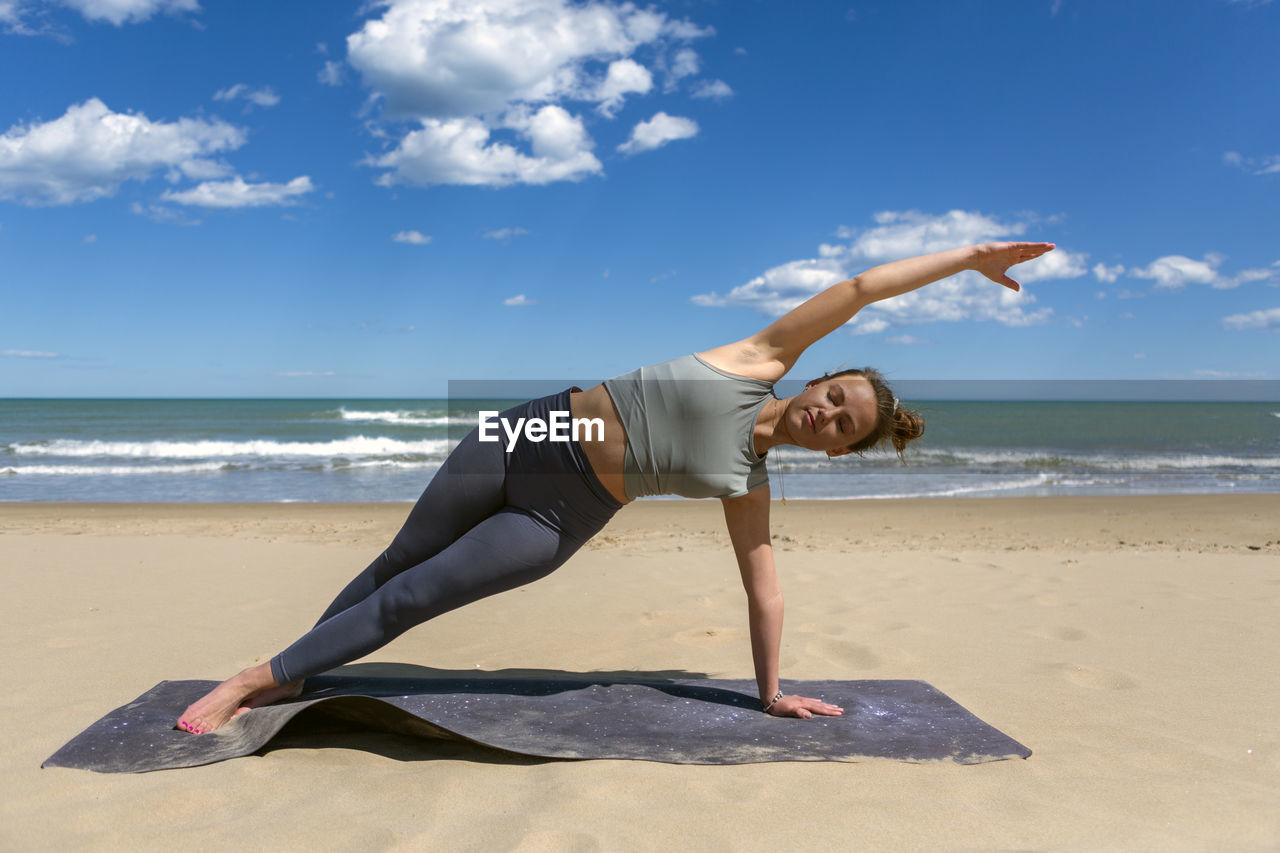 Rear view of woman exercising at beach against sky