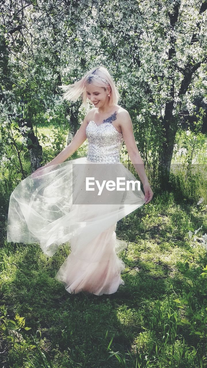 Smiling beautiful woman wearing dress while standing against trees