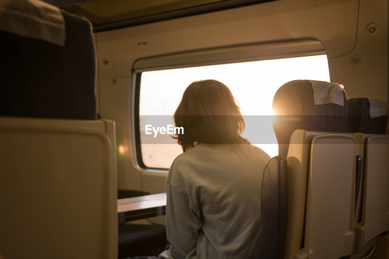 The traveling young girl looks dreamily from the window of the train into the sunrise