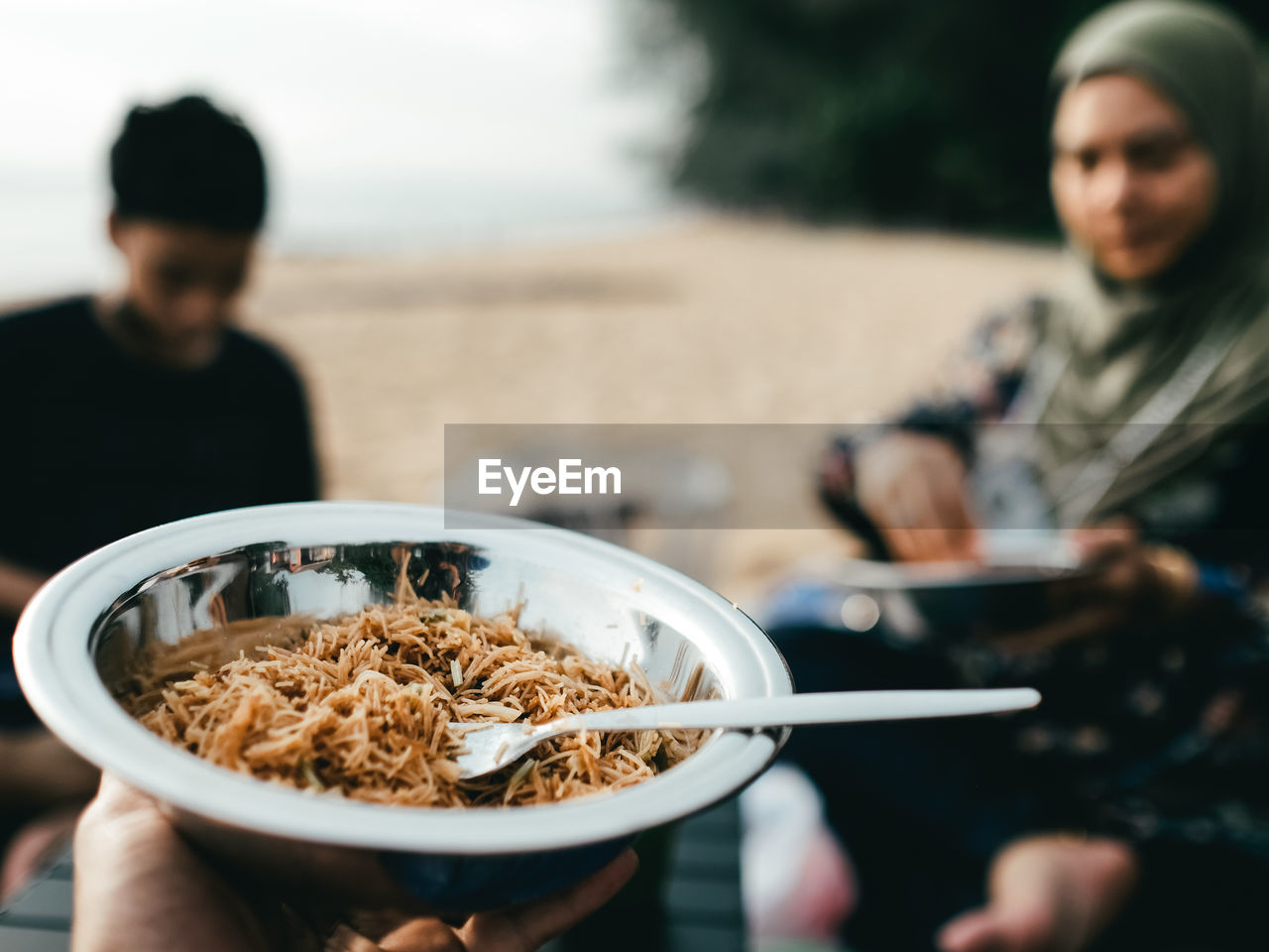 Cropped hand of man holding fried noodles on the beach