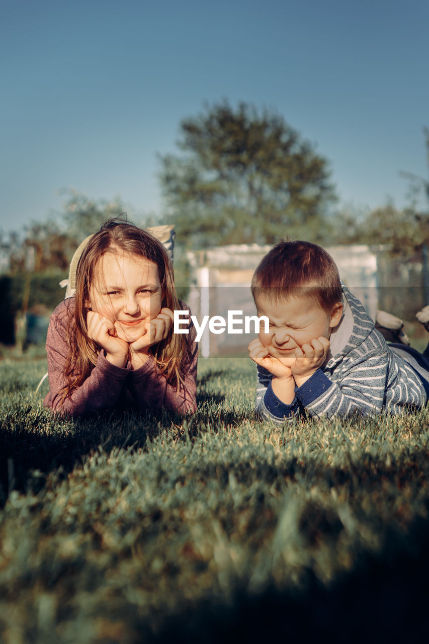 Side view of siblings on field against sky