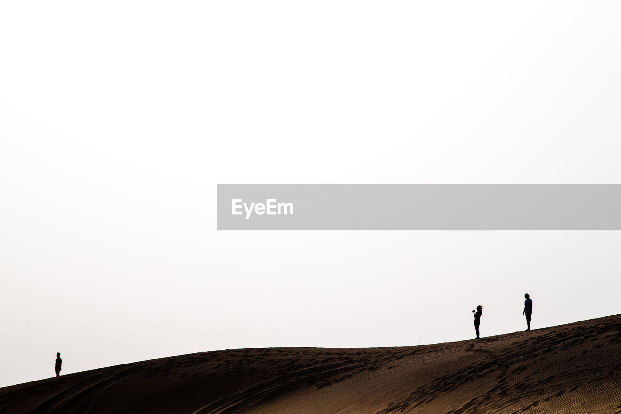 Silhouette people standing on sand dune against clear sky