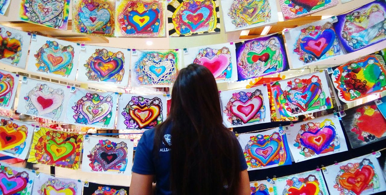 FULL LENGTH REAR VIEW OF WOMAN STANDING AGAINST MULTI COLORED WALL