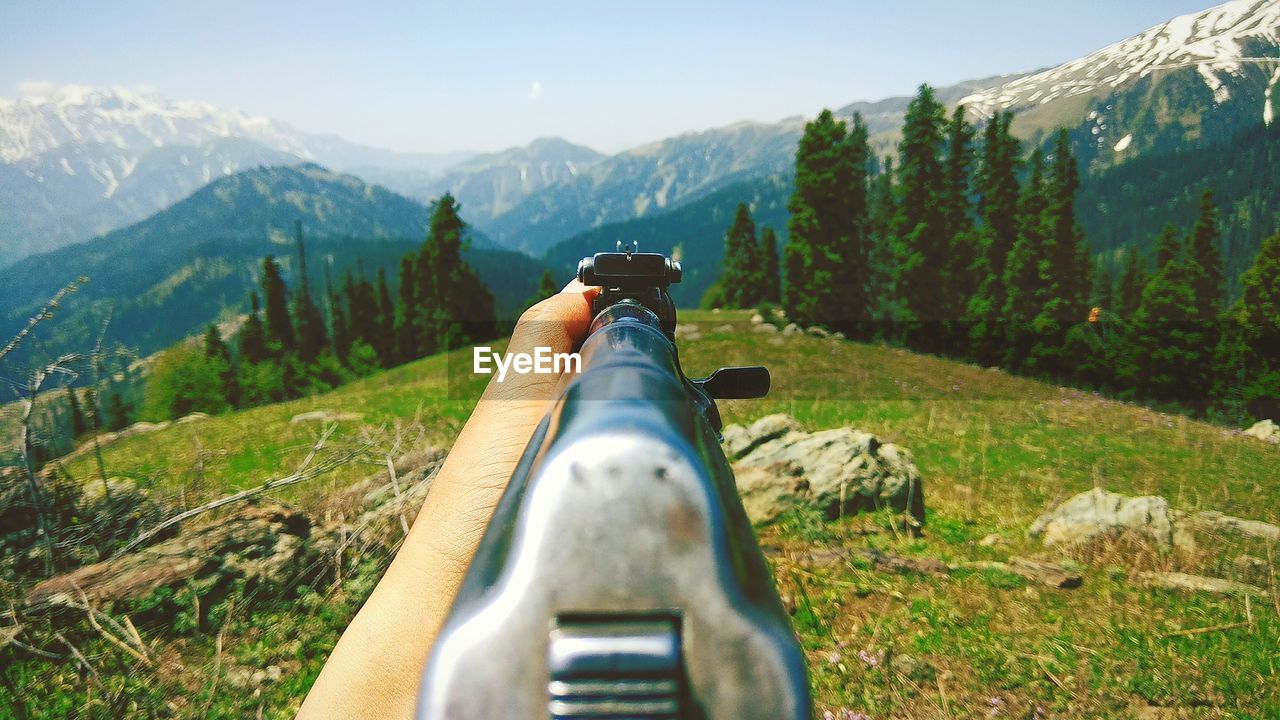 Rear view from gunpoint of man sitting on mountain against sky