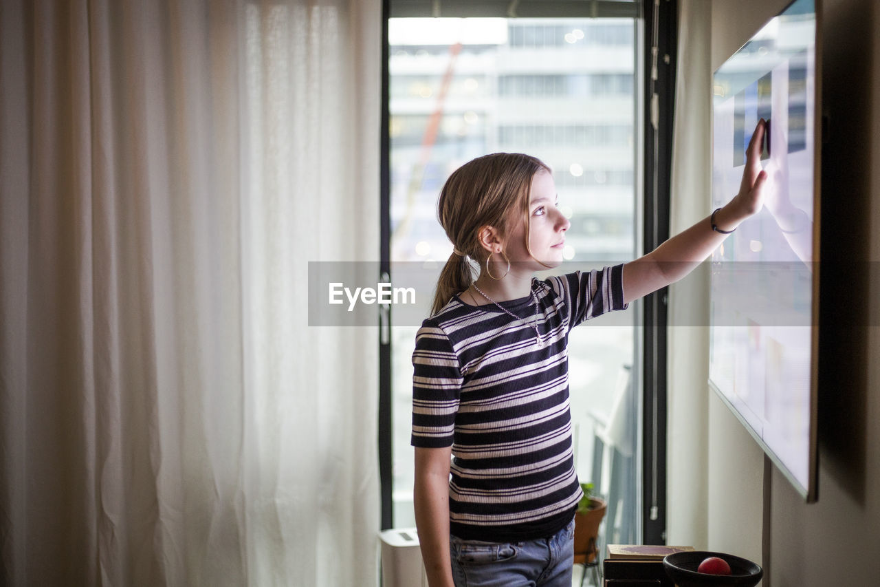 Girl touching digital display of television set at modern home