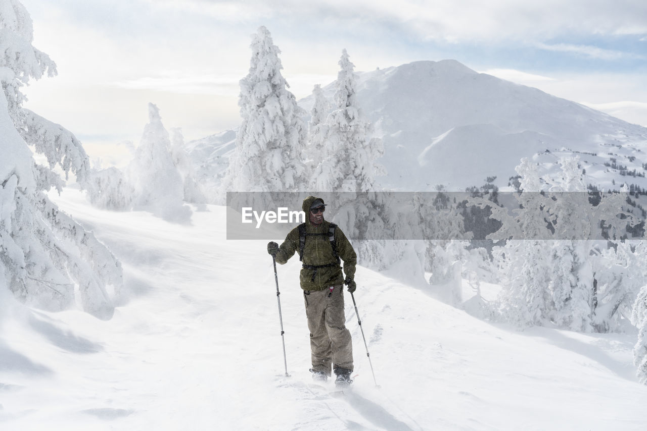 Full length of man with ski equipment standing on snowcapped mountain during foggy weather