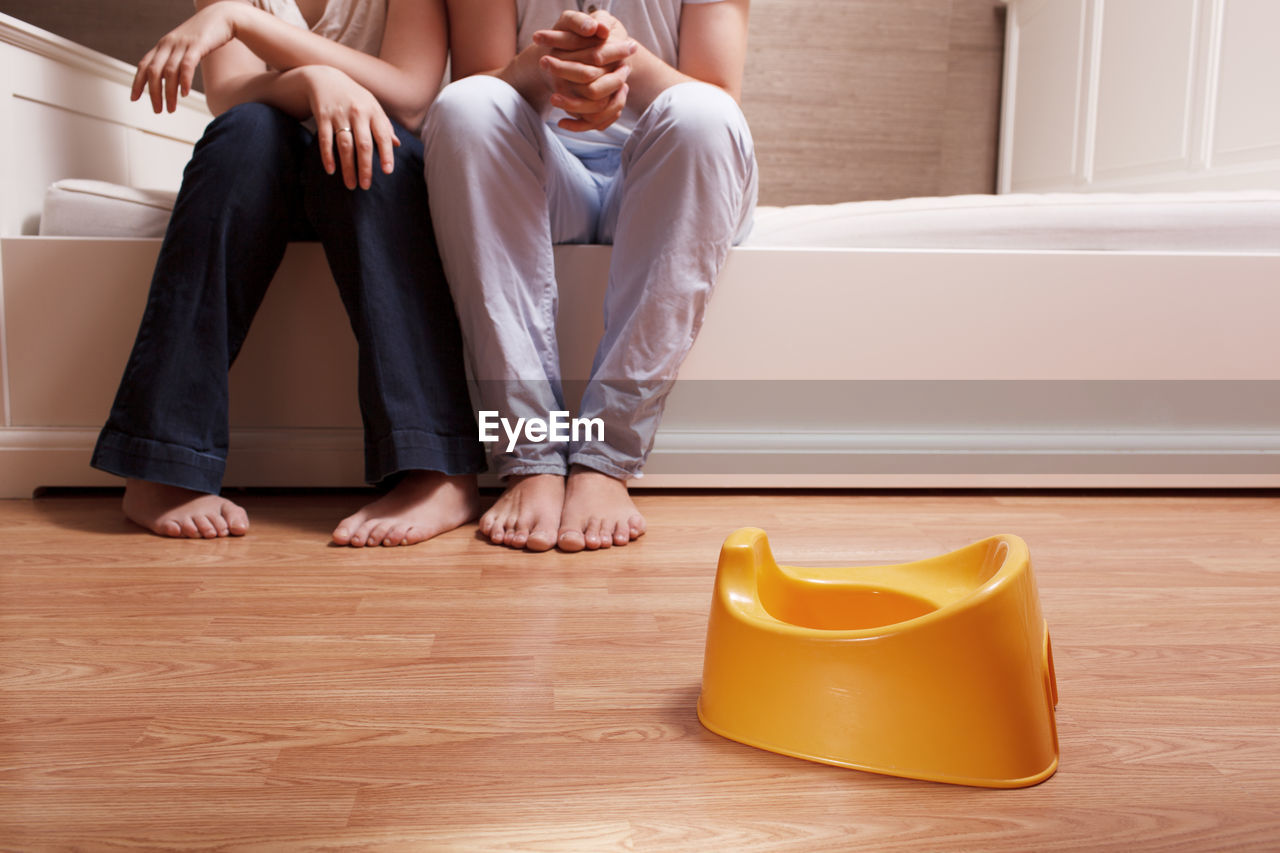 Low section of man and woman sitting on bed in front of yellow toilet bowl