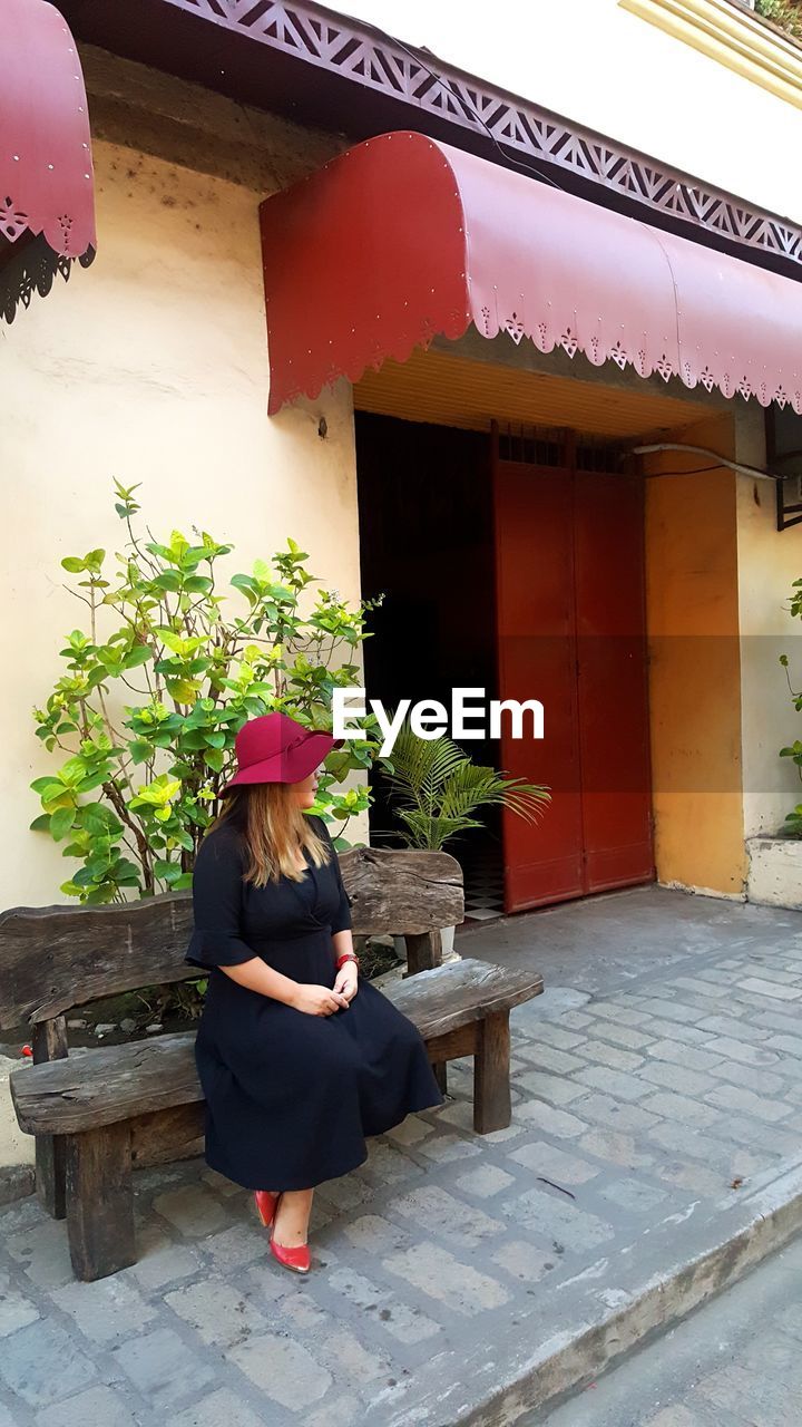 WOMAN SITTING ON BUILDING BY PLANTS