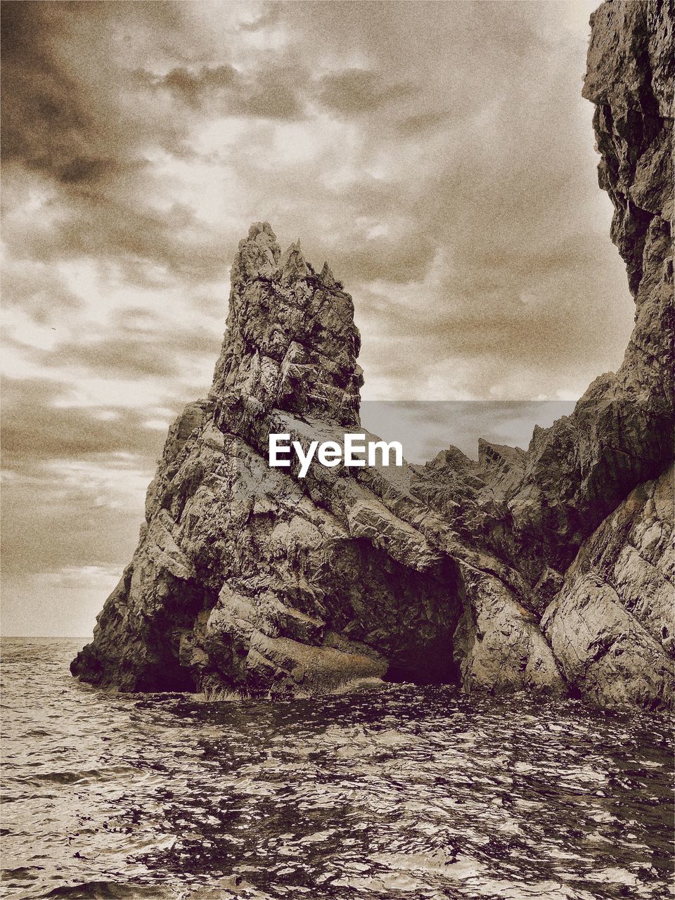 Rock formation on sea against cloudy sky