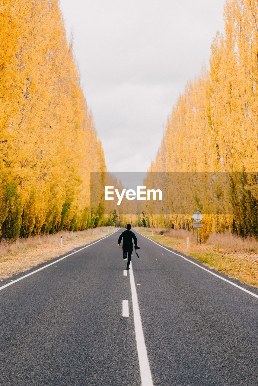 Rear view of man running on road amidst trees during autumn