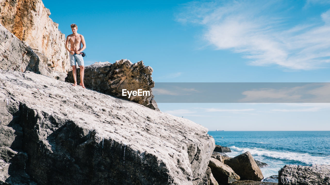 Low angle view of man standing on cliff by sea against sky