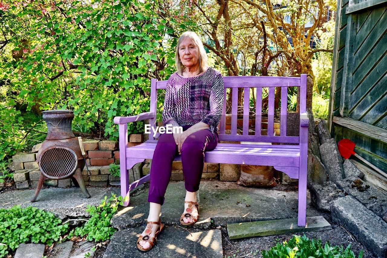 Portrait of woman sitting on bench against plants