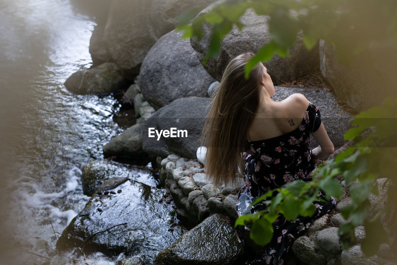 HIGH ANGLE VIEW OF WOMAN LOOKING AT ROCKS IN WATER