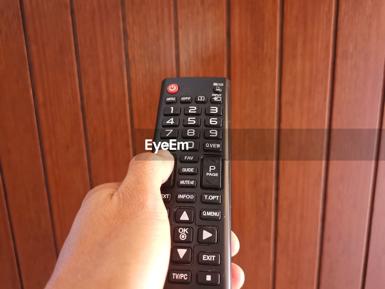 Cropped hand of man holding remote control against wall